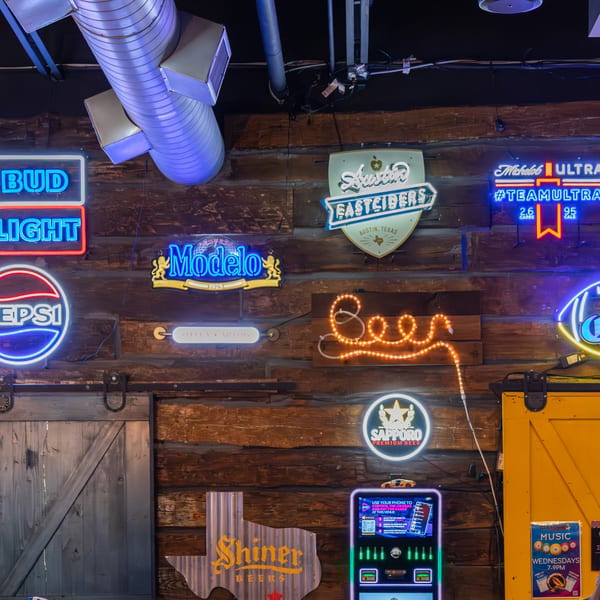 A rustic wooden wall adorned with various neon beer and soda signs, including Bud Light, Pepsi, and Modelo.