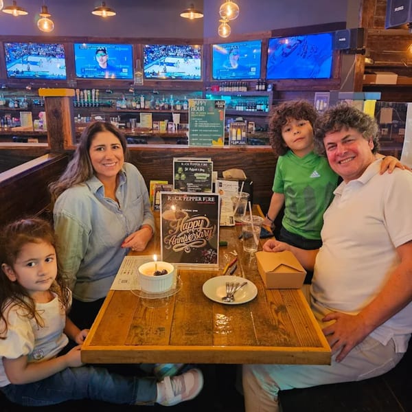Family celebrating anniversary at Rock Pepper Fire, with cake and drinks on a wooden table.