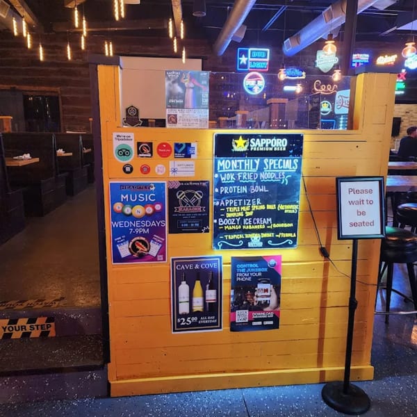 A yellow wooden partition with various signs, including Rock Pepper Fire's monthly specials and karaoke.
