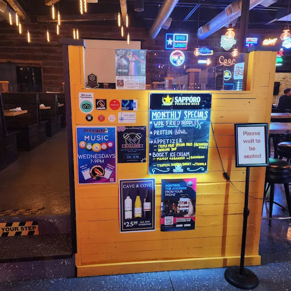 A yellow wooden partition with various signs, including Rock Pepper Fire's monthly specials and karaoke.