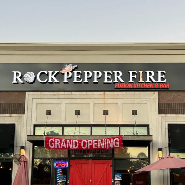 The exterior of Rock Pepper Fire restaurant with a "Grand Opening" banner and red barn doors.