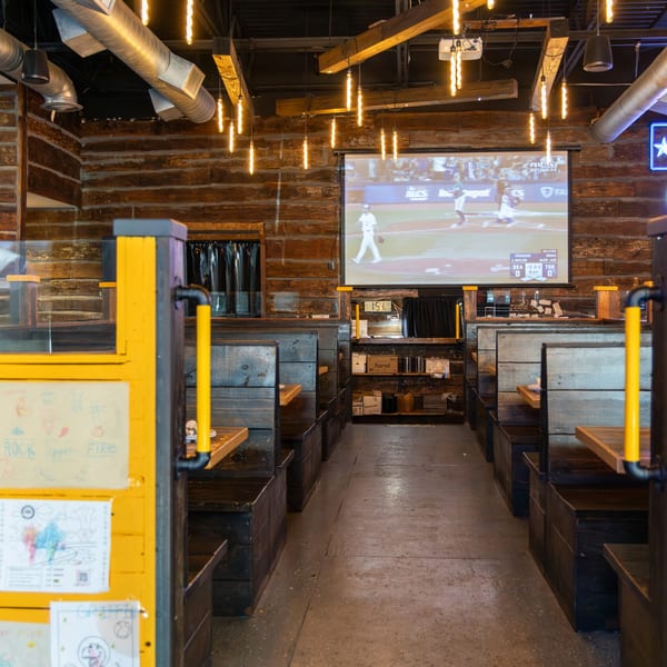 Interior of Rock Pepper Fire, a Korean restaurant, with wooden booths, a large projection screen, and industrial lighting.