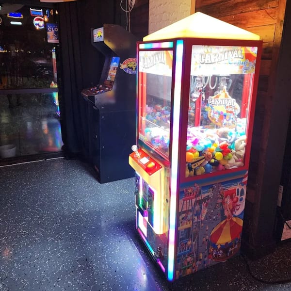 A claw machine filled with plush toys and an arcade game stand in a dimly lit room.