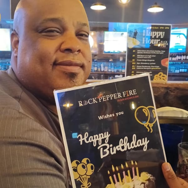 A man smiling while holding a "Happy Birthday" menu from Rock Pepper Fire restaurant.