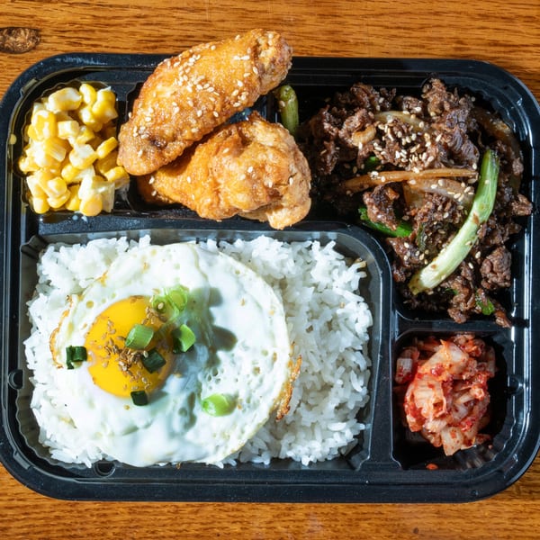 A Korean bento box with bulgogi, fried chicken, rice with fried egg, corn, and kimchi.