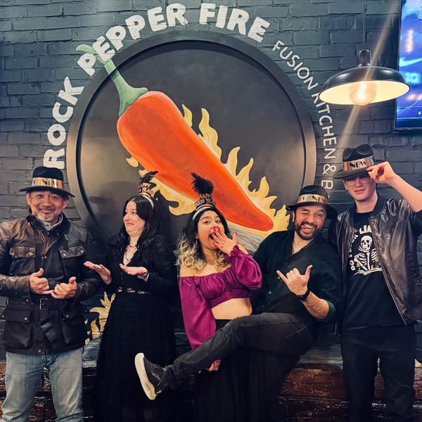 Five people posing playfully in front of the Rock Pepper Fire restaurant logo, wearing hats.