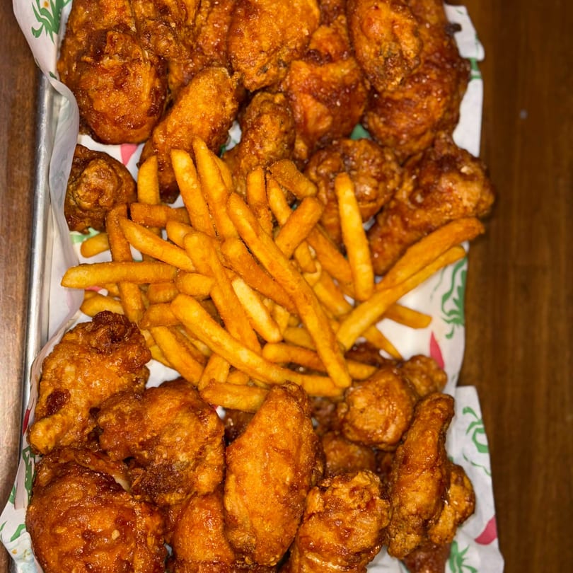 A metal tray filled with crispy, golden-brown fried chicken pieces and a pile of french fries.