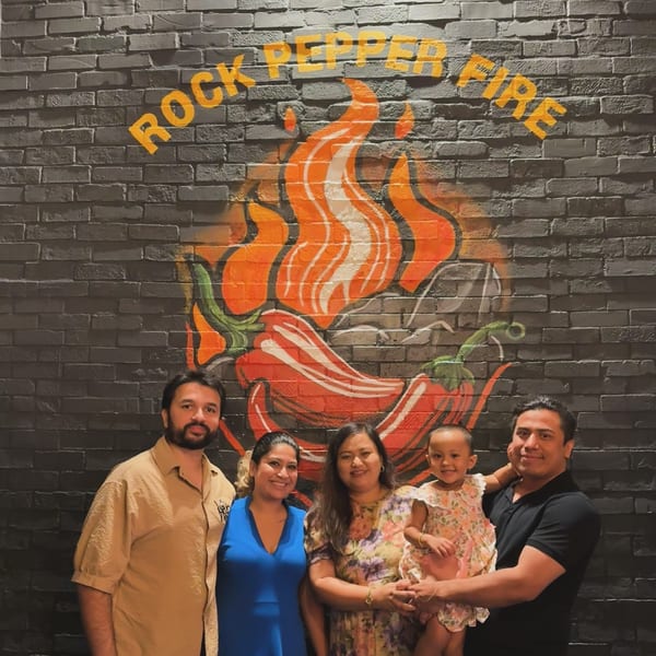 A family of five, including a baby, smiling in front of the Rock Pepper Fire logo.