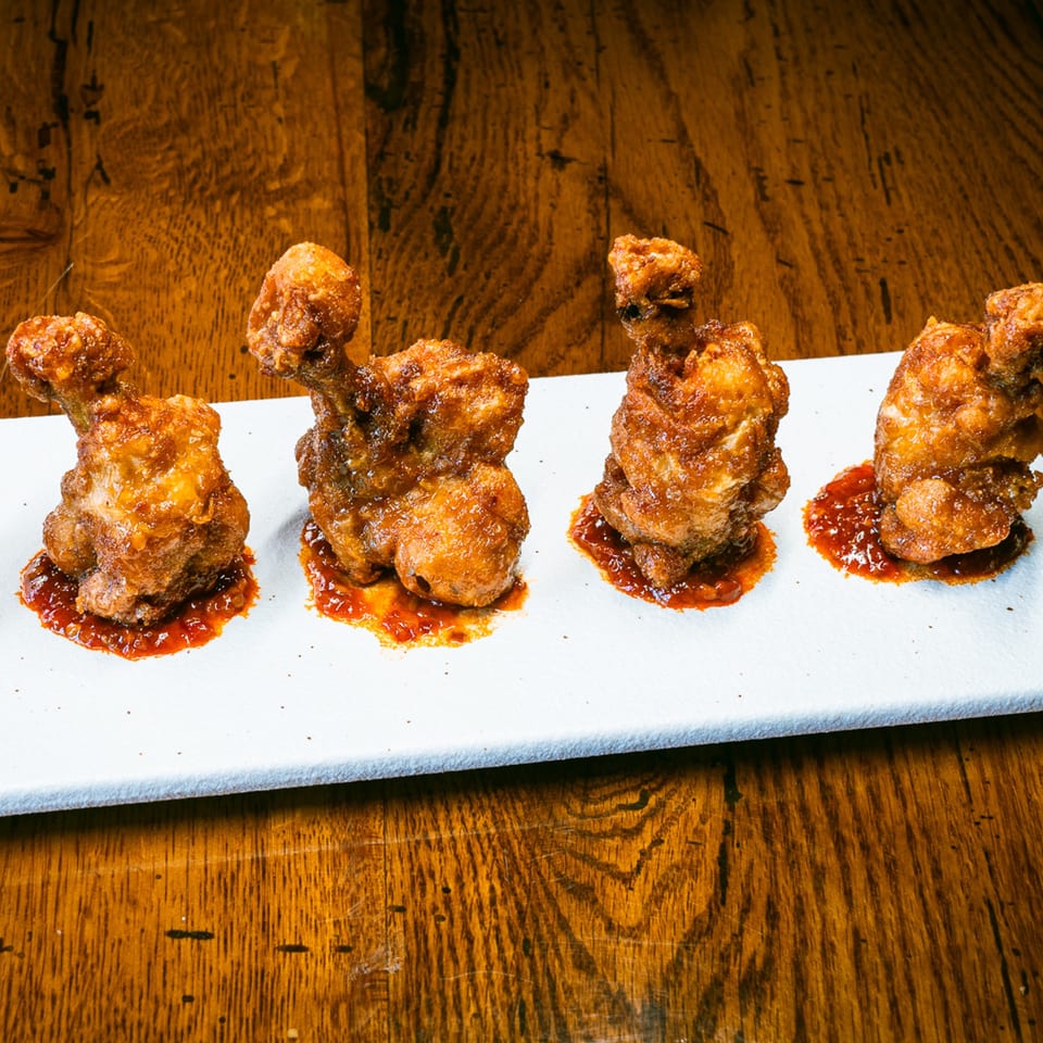 Four Korean fried chicken drumettes, glazed with spicy sauce, on a white rectangular plate.
