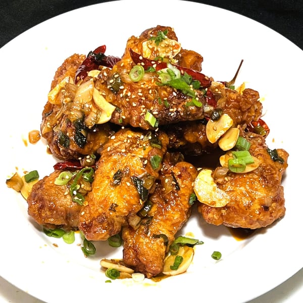 Crispy Korean fried chicken wings, glazed with sauce, garlic, sesame seeds, and green onions on a white plate.
