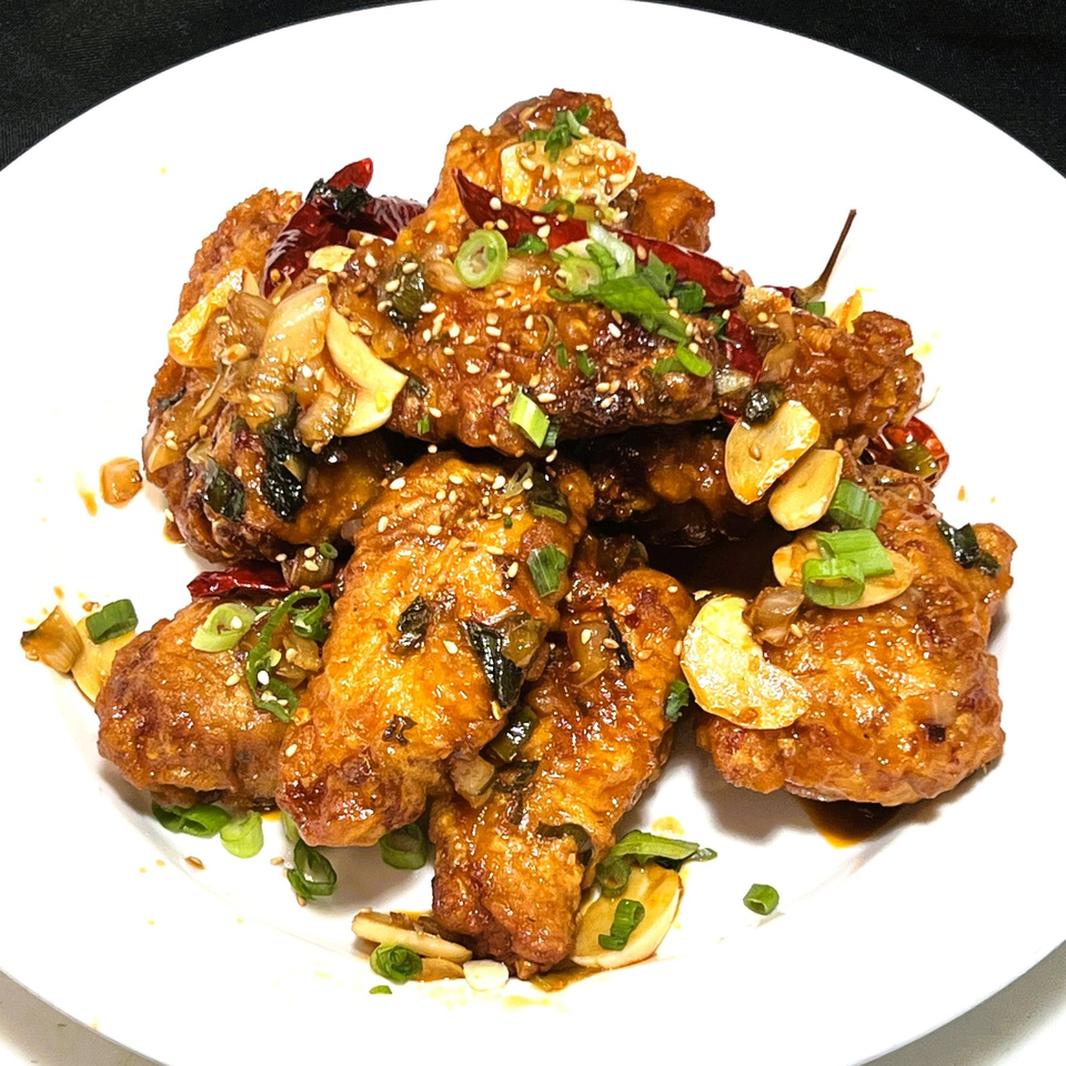 Crispy Korean fried chicken wings, glazed with sauce, garlic, sesame seeds, and green onions on a white plate.