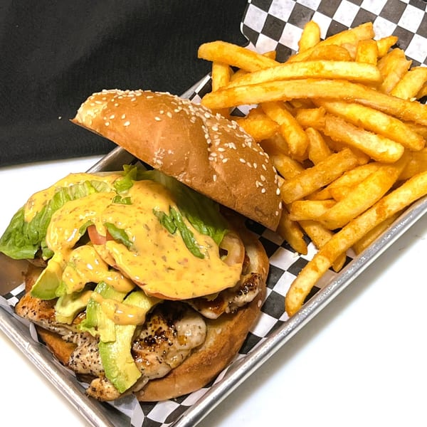 Grilled chicken sandwich with avocado, lettuce, and sauce, served with a side of french fries.
