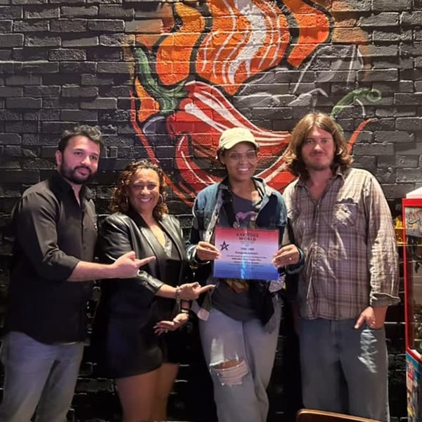 Four people pose with a "Karaoke World" award in front of a brick wall with chili pepper art.