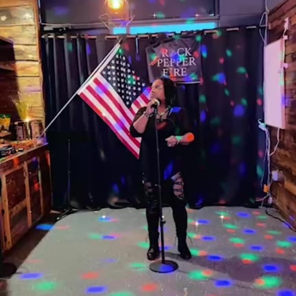 A woman sings karaoke on a stage with an American flag and Rock Pepper Fire banner.