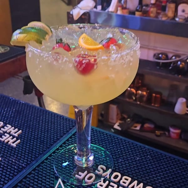 A giant margarita glass filled with a yellow drink, garnished with lime, orange, and berries.