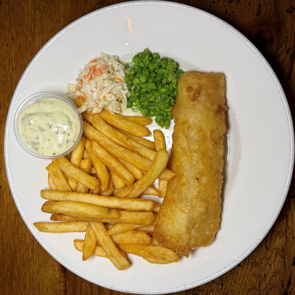 Fish and chips with coleslaw, mushy peas, and tartar sauce on a white plate.