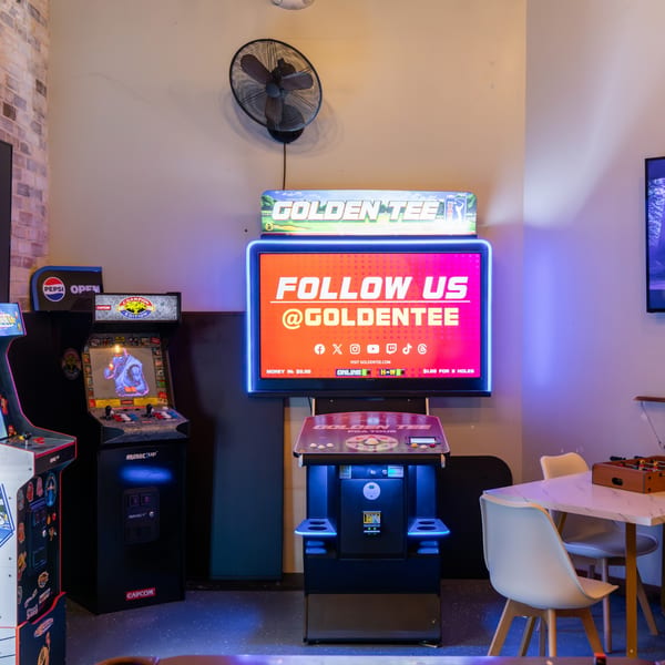 Arcade games and a Golden Tee golf simulator with a neon sign in a restaurant's game area.