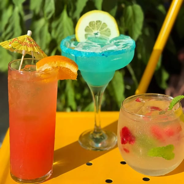 Three vibrant cocktails: a red drink with an orange slice, a blue margarita, and a clear drink with berries and mint.