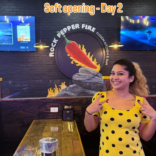 Smiling woman in yellow polka dot dress making peace signs at Rock Pepper Fire restaurant.