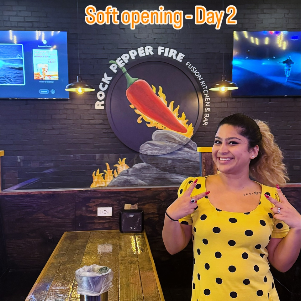 Smiling woman in yellow polka dot dress making peace signs at Rock Pepper Fire restaurant.