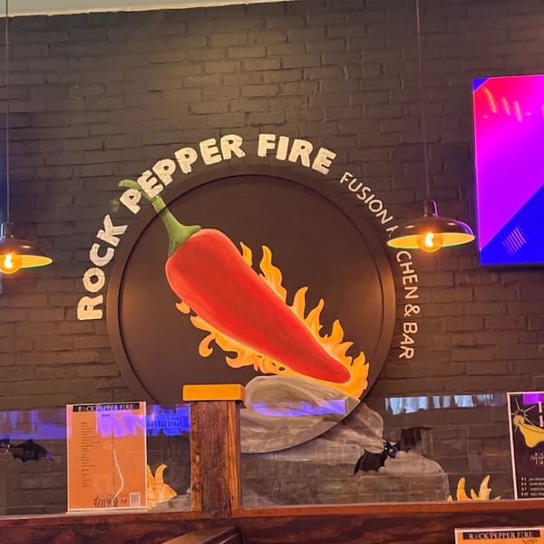 Rock Pepper Fire restaurant sign with a red chili pepper on fire against a brick wall.