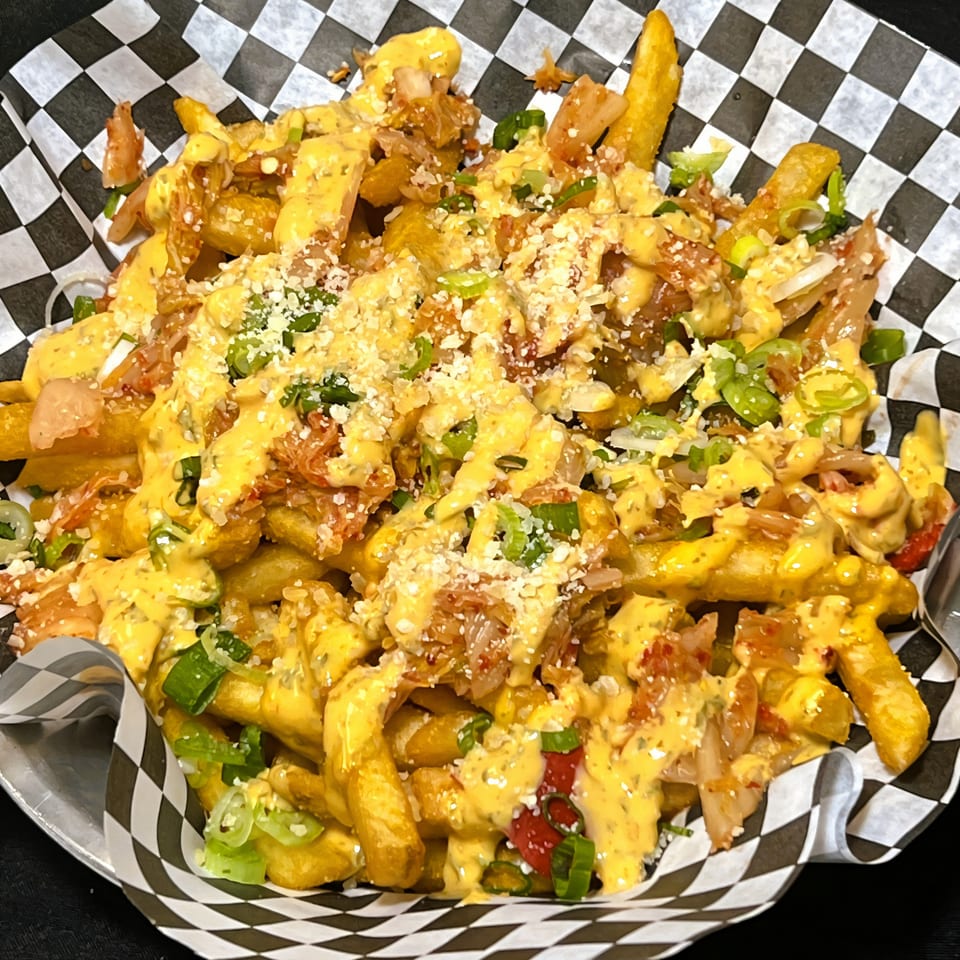 Rock Pepper Fire's Korean kimchi fries, topped with cheese sauce, green onions, and grated cheese.